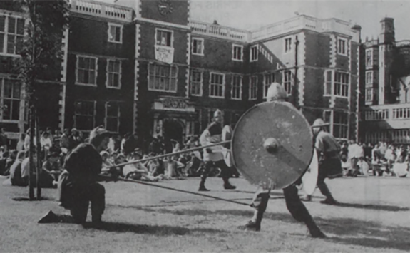 A black and white photograph showing students on campus performing in a medieval jousting competition