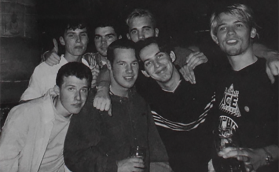 A black and white photograph of 7 male students with arms round each other on a night out