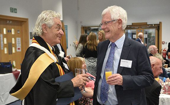 Two male alumni chatting and holding drinks