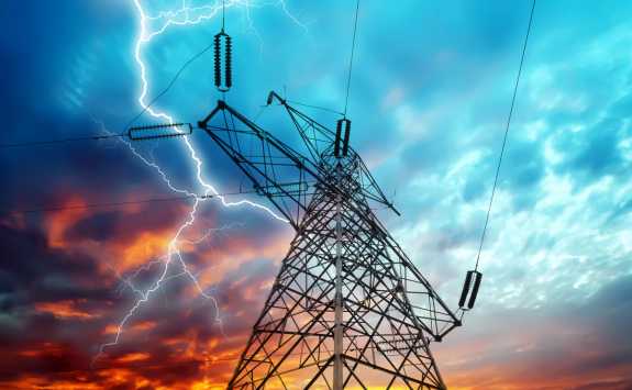 Lightning strikes near a power transmission tower at dusk, highlighting electrical infrastructure.