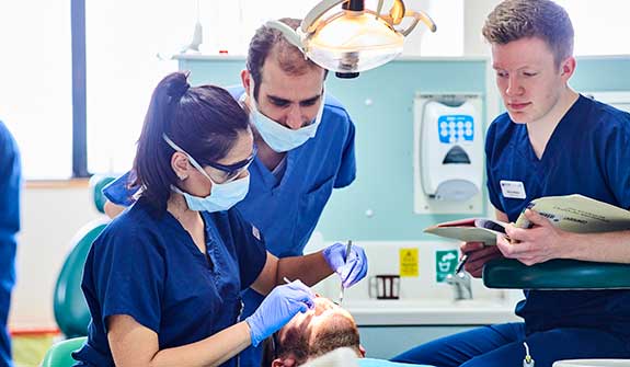 Students working on a dental patient in a clinical scenario under the expert guidance of a clinician.