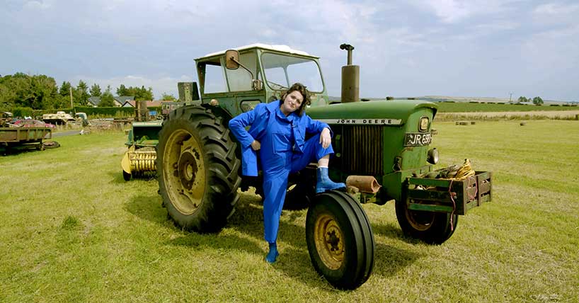the image shows a woman standing next to a tractor. 