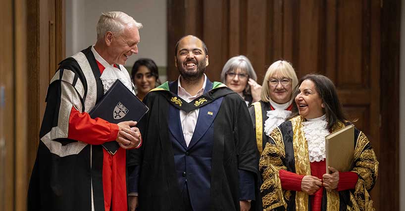 Procession exiting ceremony with participants in red, black and gold University gowns and Professors Ambani, Day laughing with Chancellor Imtiaz Dharker Procession exiting ceremony with participants in red, black and gold University gowns and Professors Ambani, Day laughing with Chancellor Imtiaz Dharker