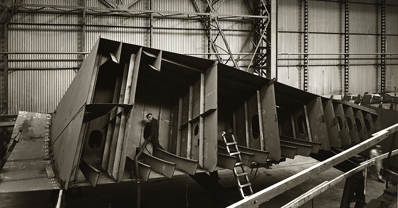 A black and white photo showing a man constructing the hull of a steel ship