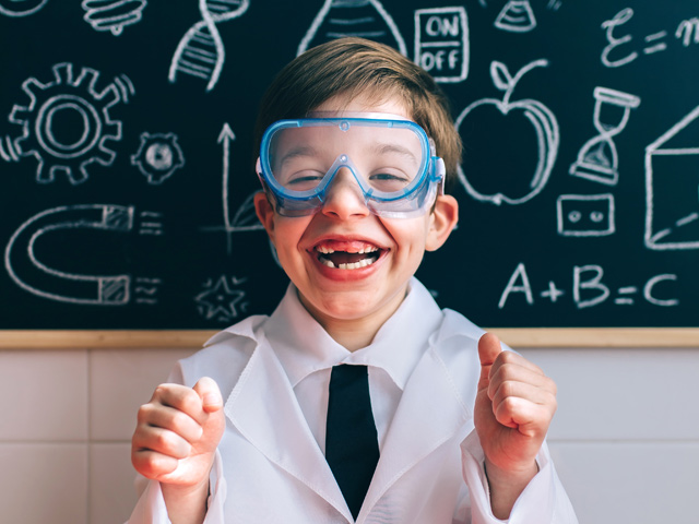 A young schoolboy wearing a lab coat and goggles, excited by a science experiment. 