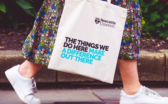 A visitor walking through the Newcastle University campus. She is carrying a bag that reads, "The things we do here make a difference out there."