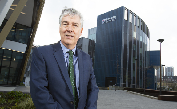 Paul Brannen stands in the Helix with a building in the back with the Newcastle University logo on it