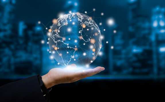 An open hand holding a CGI globe covered in points of light which make up a business network. 
