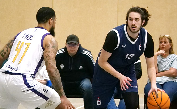 Austin Sacks facing an opposing player while dribbling a basketball during a game for Newcastle University