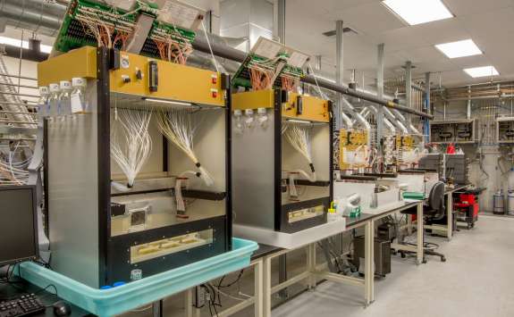 A modern biotechnology lab with multiple chromatography machines lined up, equipped with computer interfaces and various lab equipment.