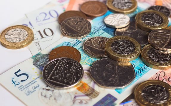 British pound banknotes and assorted coins scattered, showcasing various denominations including £5, £10, £20 notes, and one-pound coins.