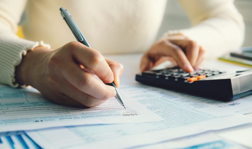 Person using a calculator and filling out financial forms at a desk, with a focus on hands.