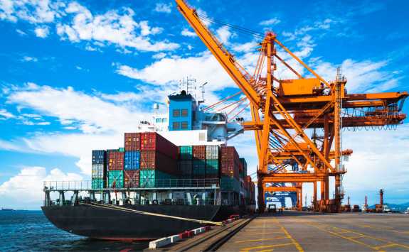 A container ship in dock being loaded by a large yellow crane