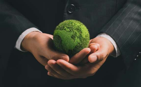 Person in business attire holding a green globe of the Earth made of grass