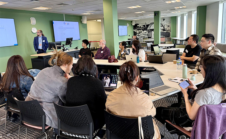 A diverse group seated around tables with laptops, listening to a speaker presenting slides during the Finance Research Festival