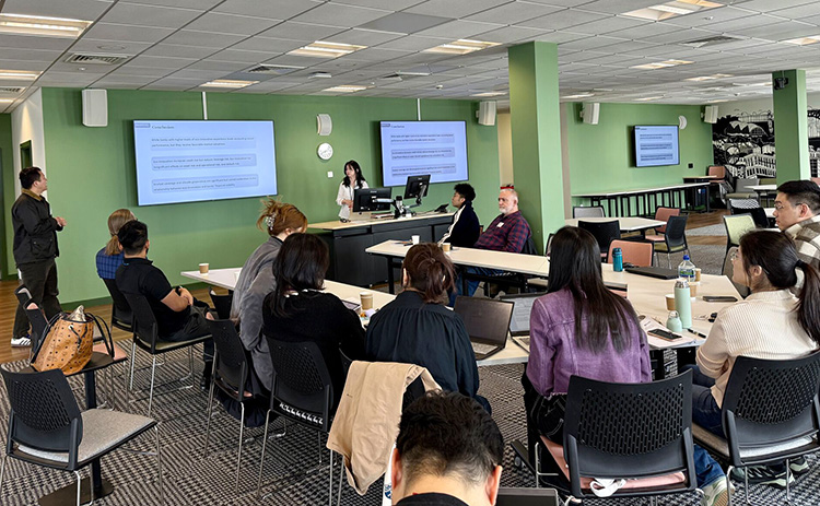 A postgraduate student stands at the front of St James View presenting slides to a seated group during the Finance Research Festival at Newcastle University