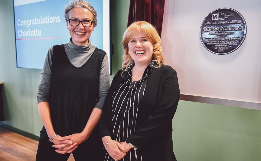 Lucy Hatt and Charlotte Windebank smiling at the Women in Innovation Award ceremony, with the plaque displayed on the wall in the background.
