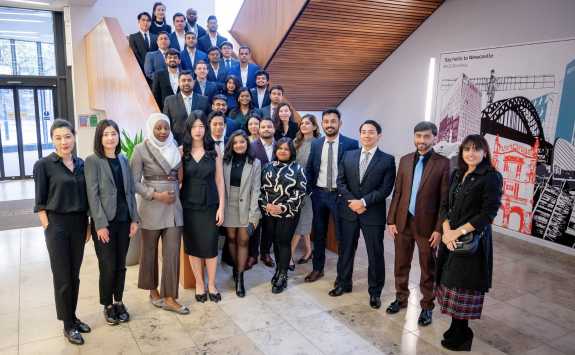 The Newcastle University Business School MBA cohort for 2023-24 standing on the stairs in the Business School foyer. 