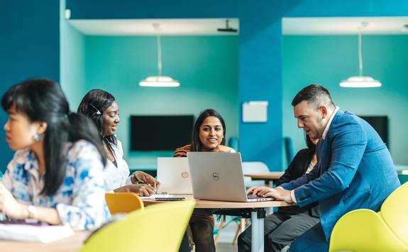 A group of MBA students sit and work together on laptops