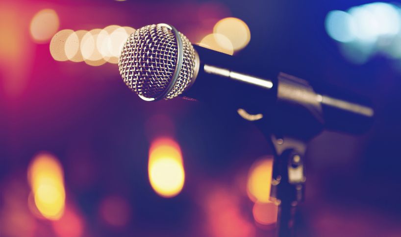 Close-up of a microphone on a stand with colourful blurred stage lights in the background.