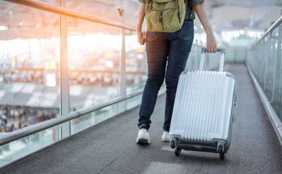 A Business School student wheeling luggage across an airport jet bridge