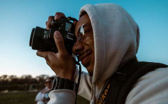 A photographer in a grey hoodie taking a photo with a DSLR camera held up to his eye