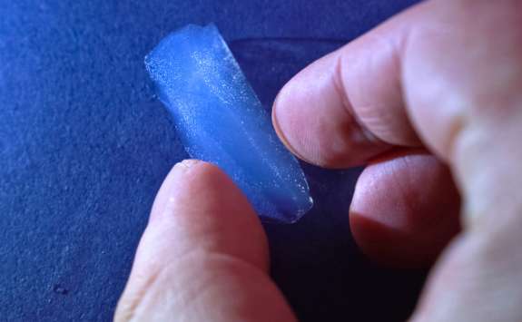 A translucent blue silica aerogel slab is held between fingers, showcasing its lightweight and fragile structure.