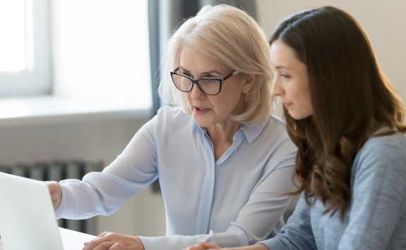 A female business mentor working at a laptop with a younger female mentee