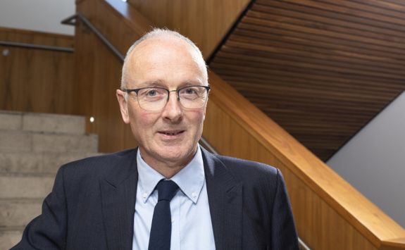 Professor Stewart Robinson wearing a dark suit standing on the stairs at Newcastle University Business School