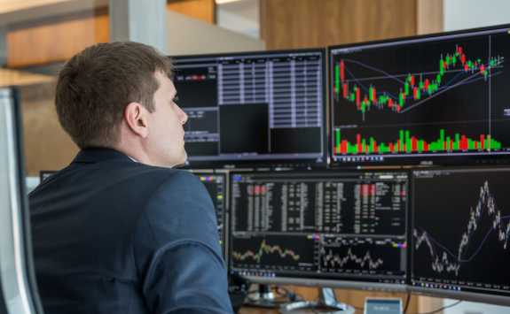 Trader analysing multiple stock market graphs on computer screens.