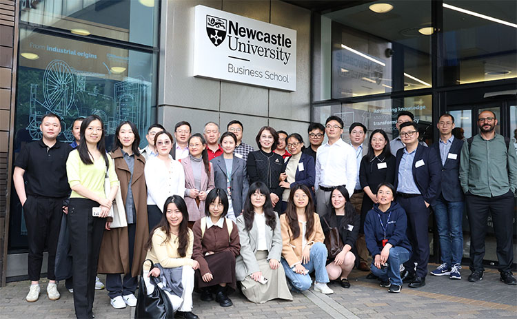 Group photo of Tri-University Conference attendees standing in front of Newcastle University Business School main entrance