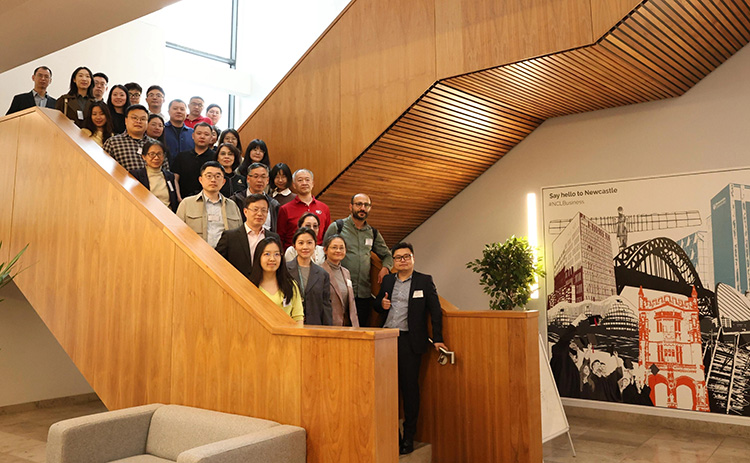 Group photo of Tri-University Conference attendees standing on the stairs in Newcastle University Business School