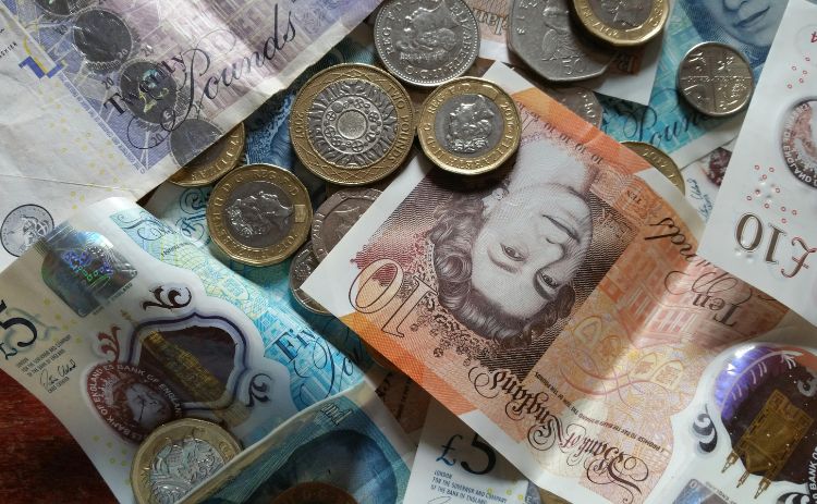 Close-up of British currency, including £5, £10, and £20 notes, along with one-pound and other coins scattered on a surface.