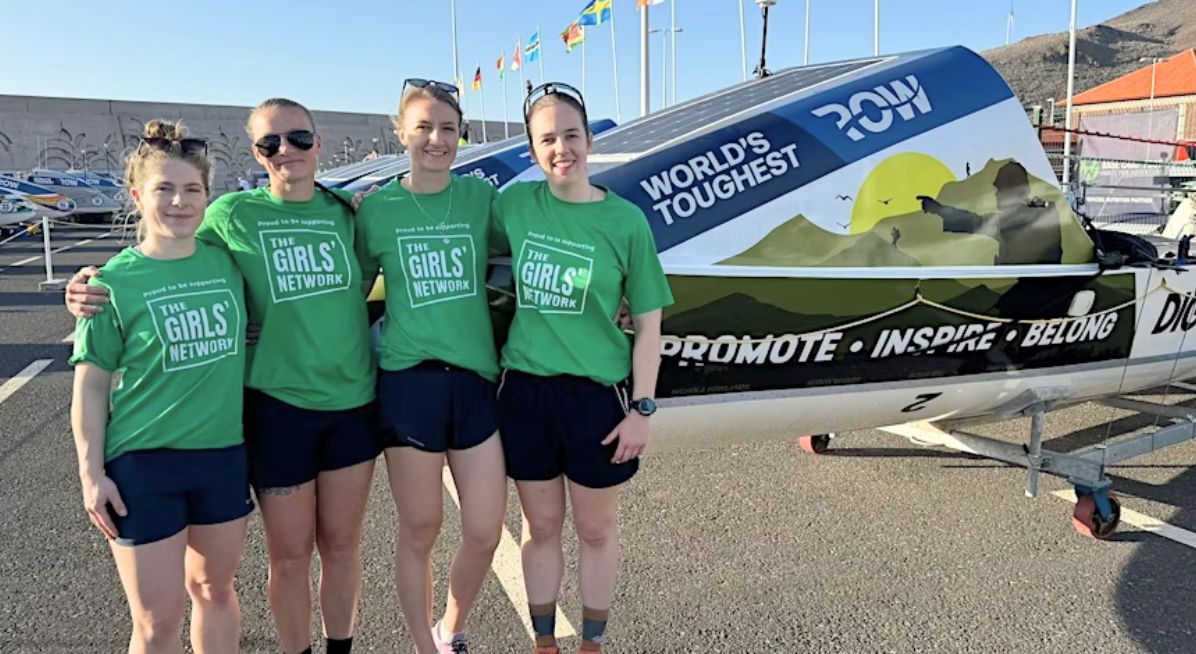 Four women in green T-shirts stand in front of a rowing boat