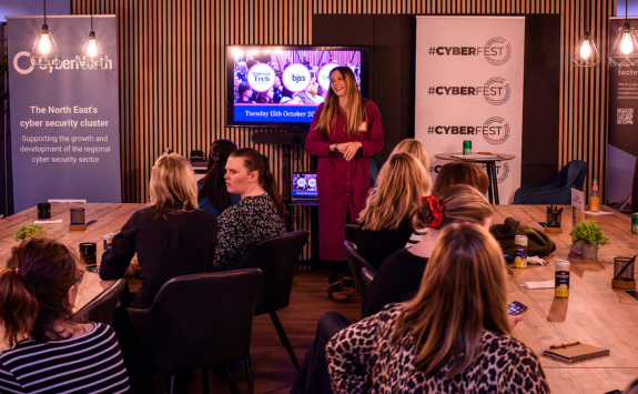 Rachel Pattinson stands in front of a tv, presenting to a crowd