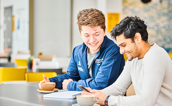 Two students sit together enjoying a coffee in the Urban Sciences Building cafe.