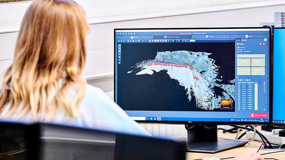 Geospatial student sitting behind a computer, mapping a piece of land. 