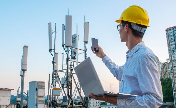 A man standing by mobile tower with a mobile phone.