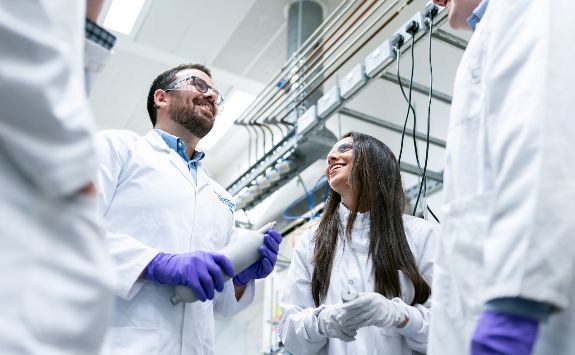 A group of people wearing lab coats having a discussion inside a laboratory.