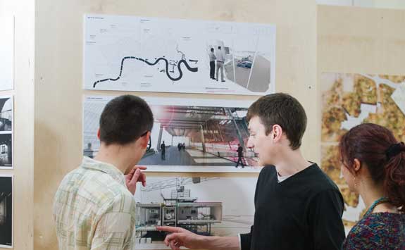 three students looking at an architectural drawing on the wall
