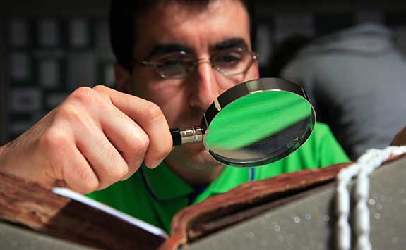 A postgraduate inspects a historic text with a magnifying glass.