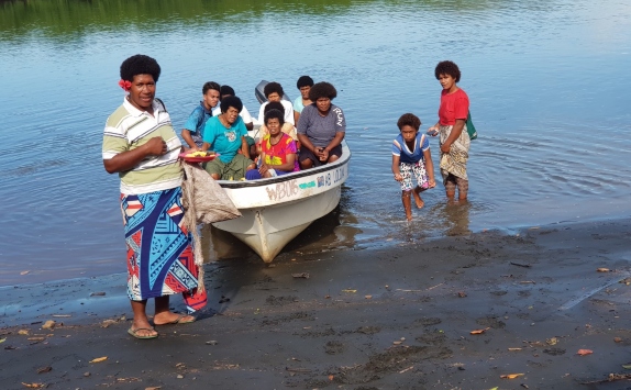 A group of Fijian people sitting in a boat on a shore, preparing to go crab fishing
