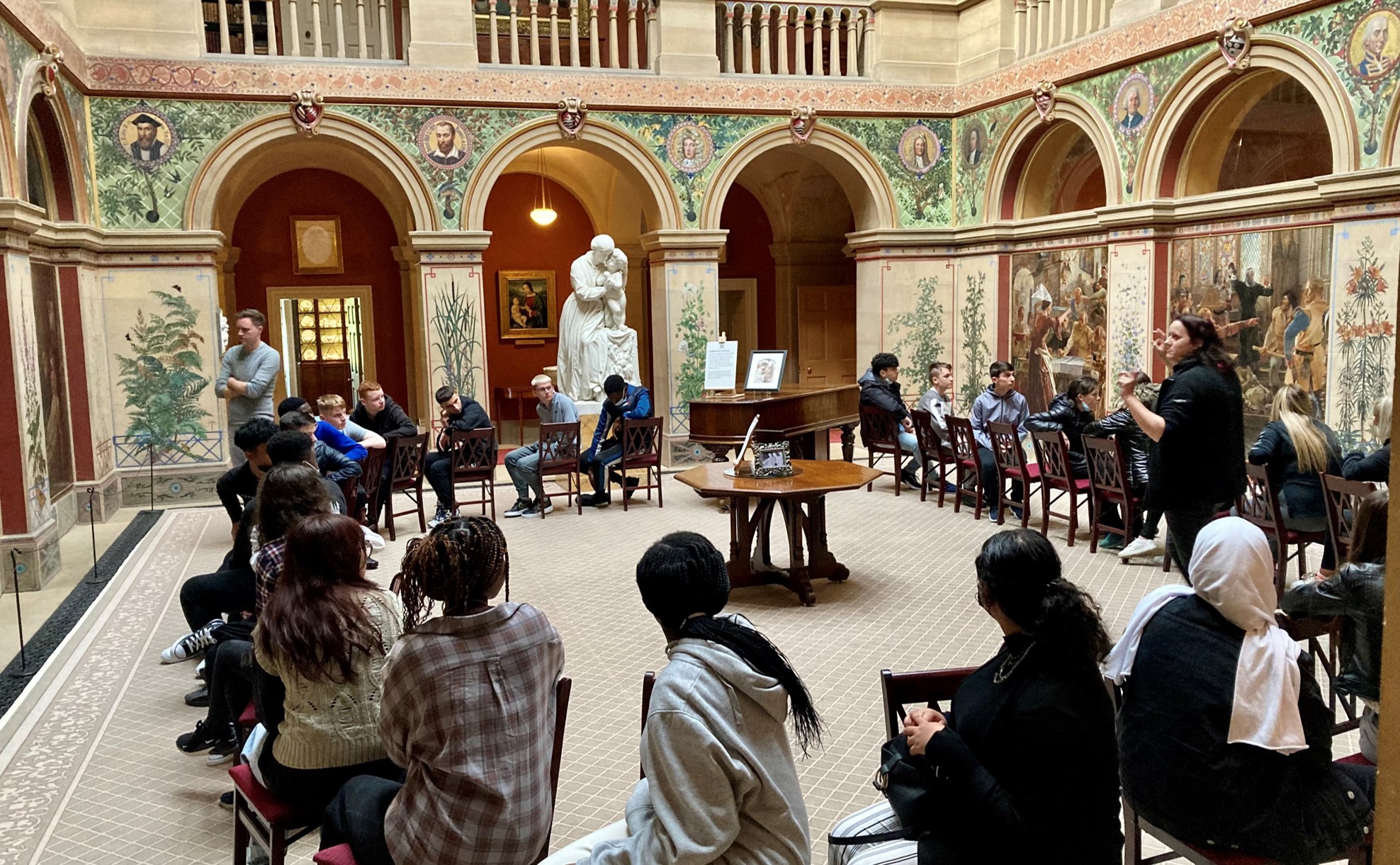 Students sitting in a circle listening to a tour guide at Wallington Hall, a National Trust property in Northumberland
