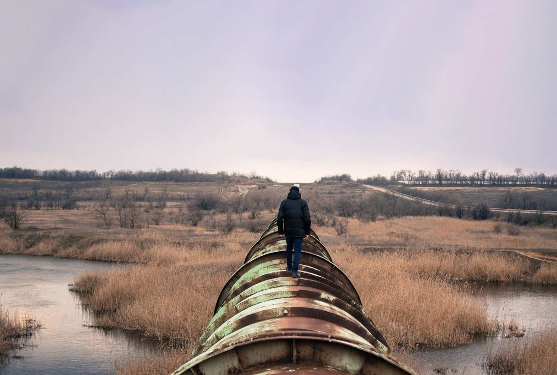 A Man walking away from the camera, on a large pipe.