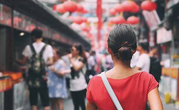 A woman seen from the back, walking through a busy street reminiscent of a South East Asian city