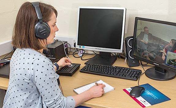 Woman wearing headphones taking notes.