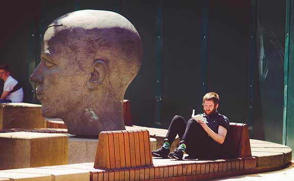 Man reading whilst sitting on a bench outdoors.