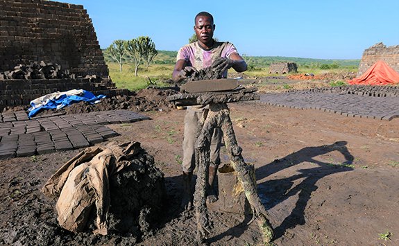 Artist working on sculpture outside with East African landscape behind him 