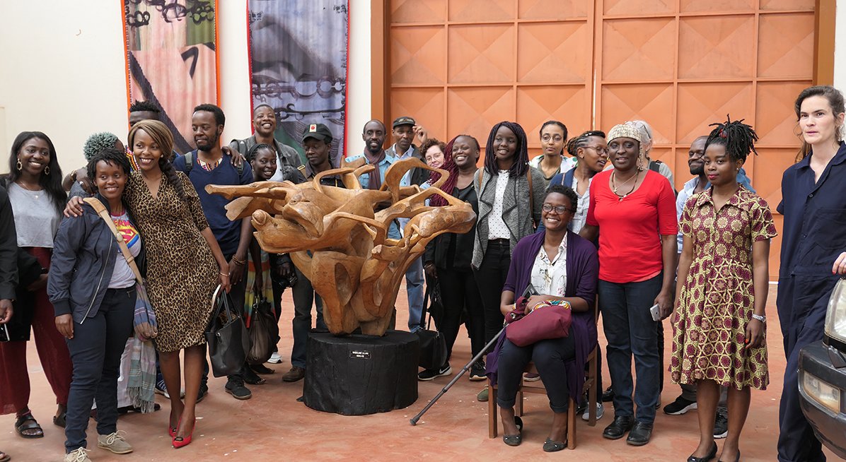 Group of artists standing around a wooden sculpture and posing for a photograph