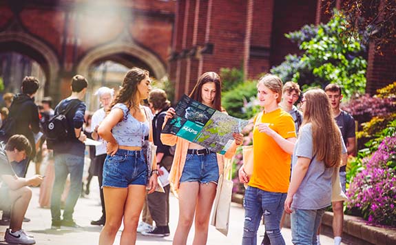 Young women looking at a map on Newcastle University campus, as an Open Day guide gives them directions.